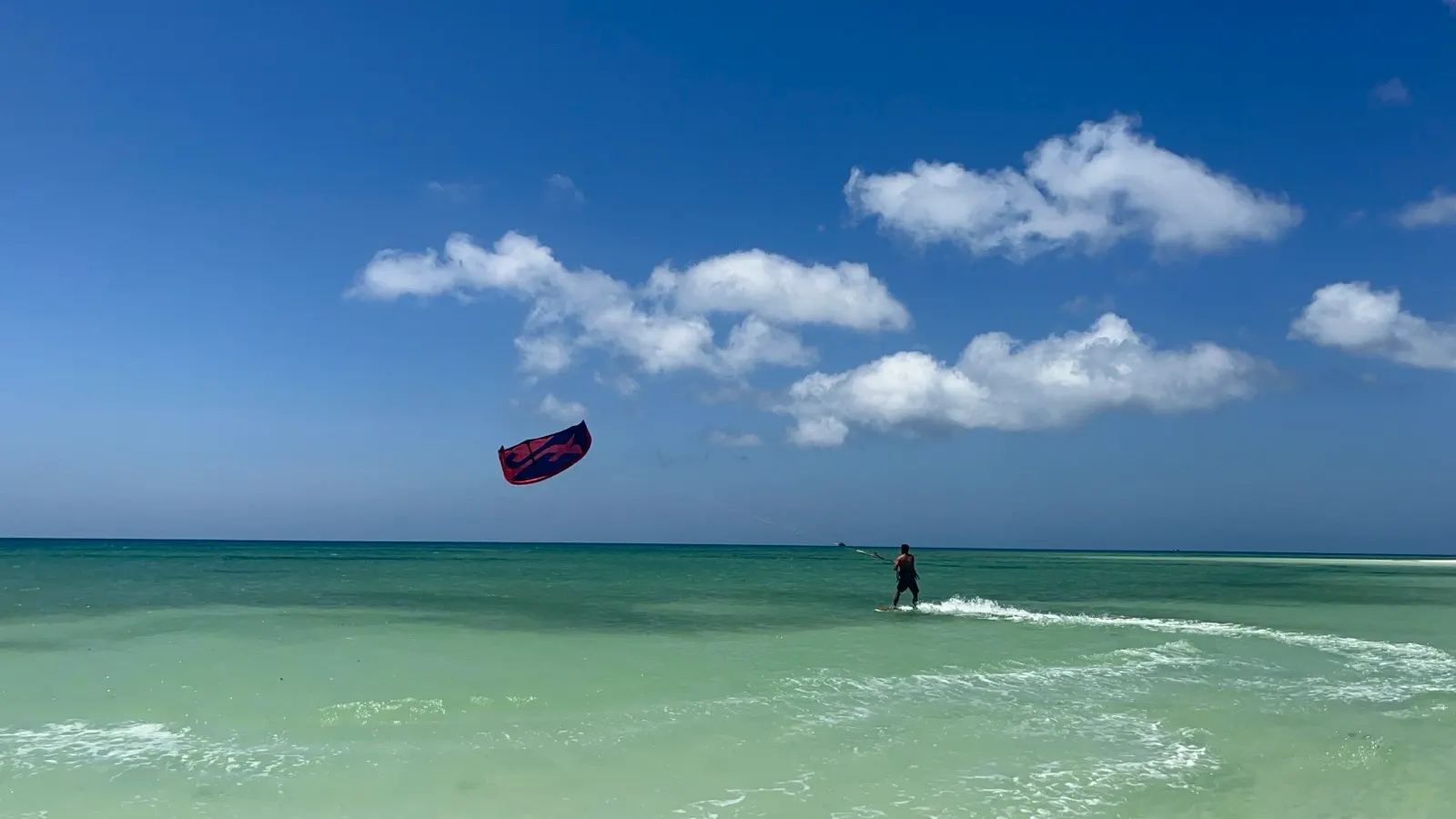 Kitesurfer riding with kite against blue sky