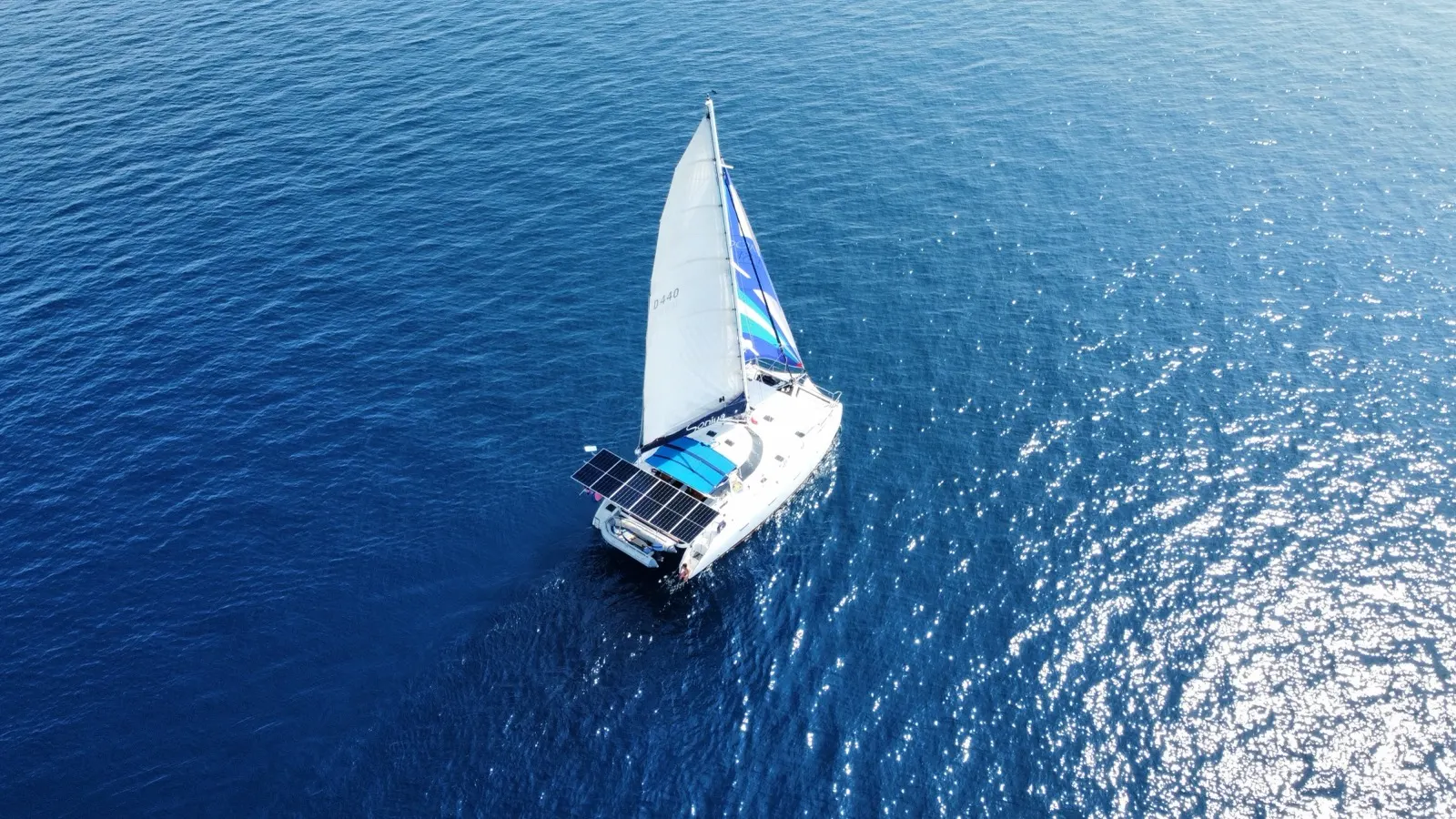 Two women waving from bow trampoline under spinnaker