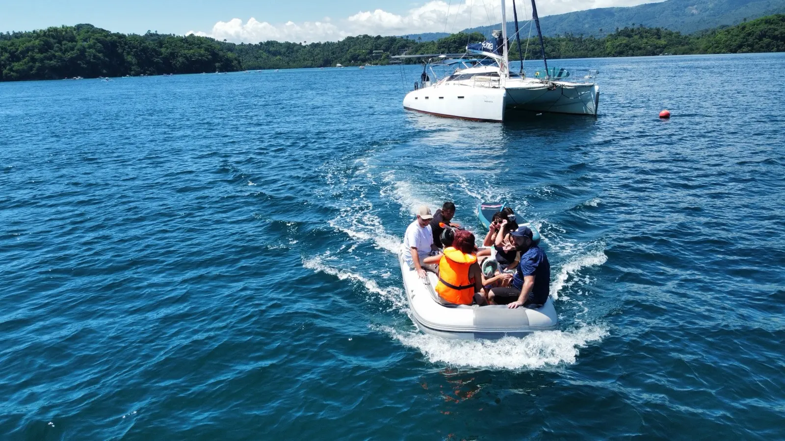 Group riding dinghy towing paddleboard, catamaran distant