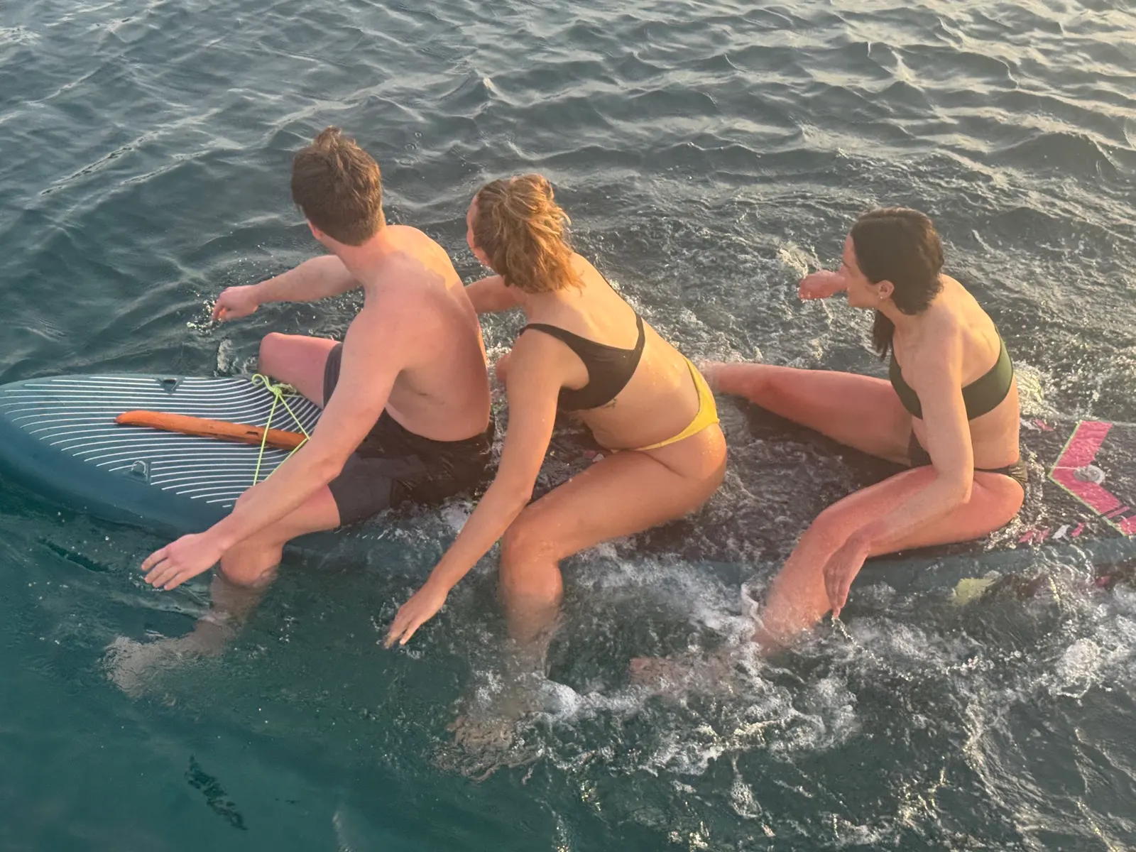 Three friends sitting together on paddleboard at sunset