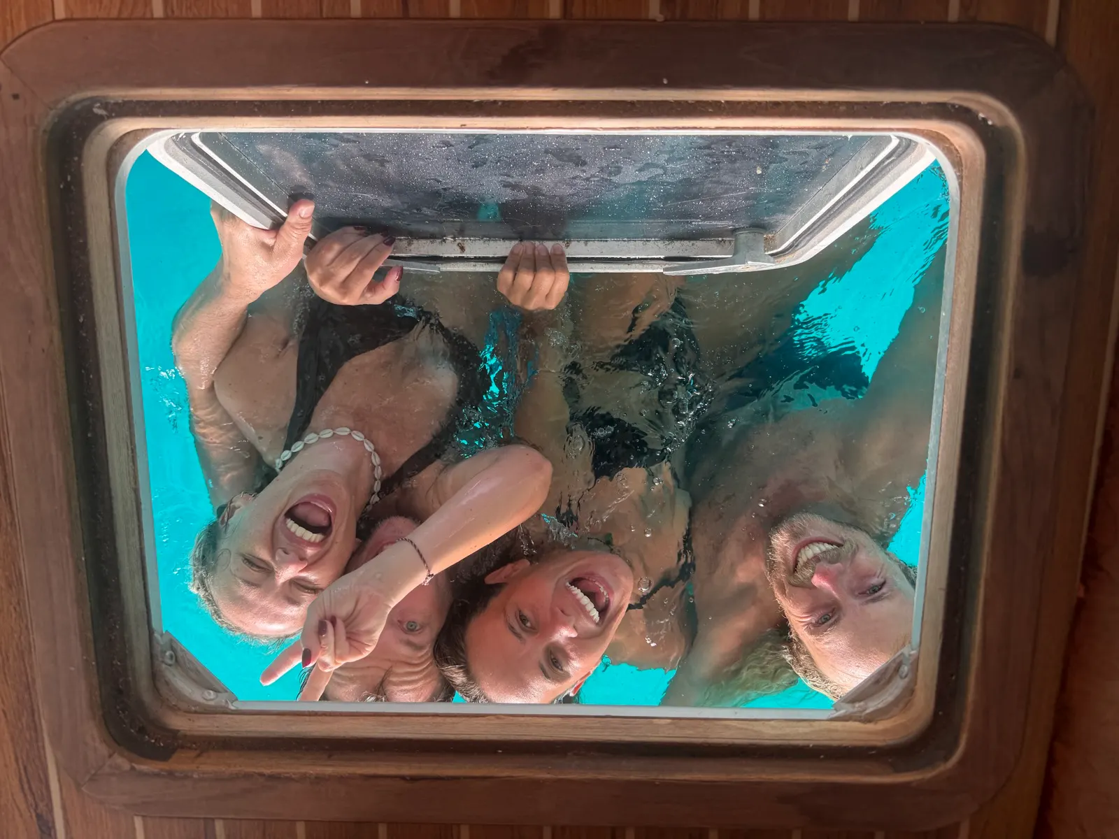 Four friends laughing, underwater selfie through porthole