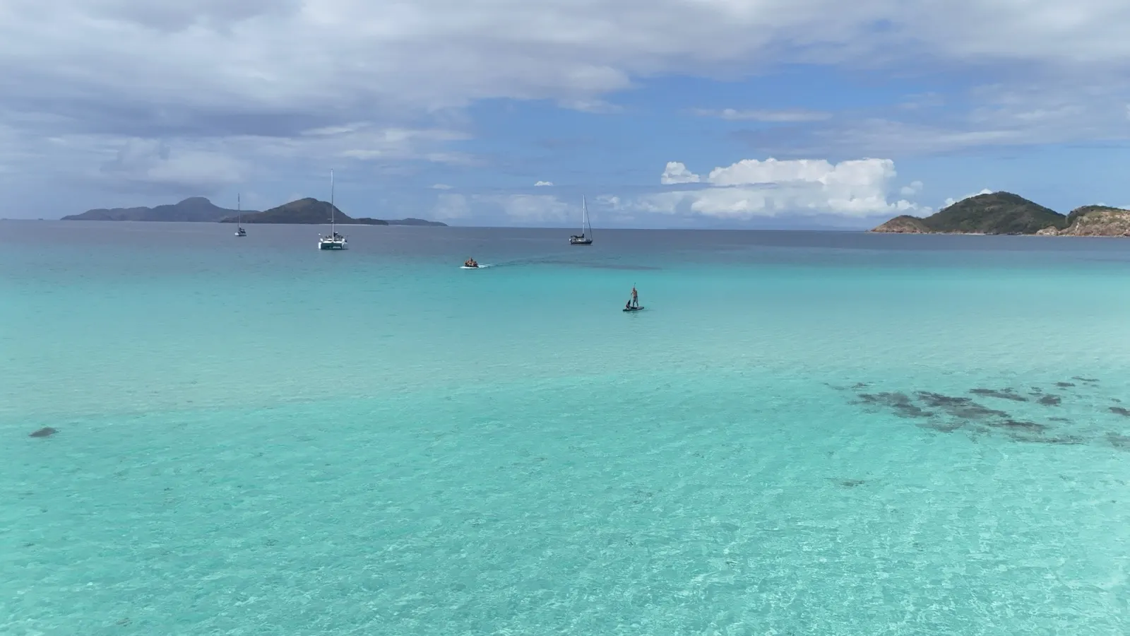 Group in dinghy towing paddleboard, sailboats distant