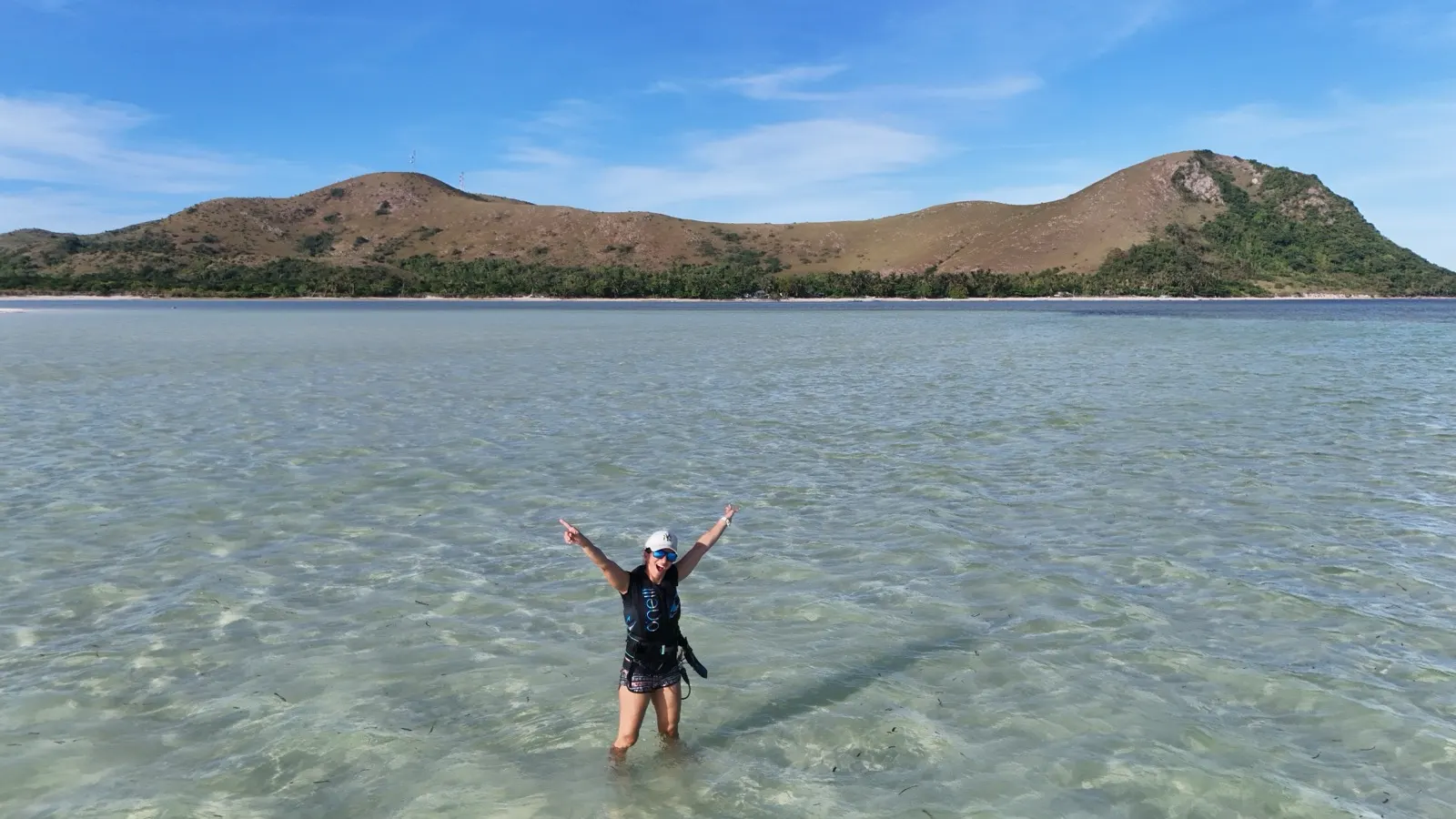 Woman cheering arms-up in shallow water, hills behind