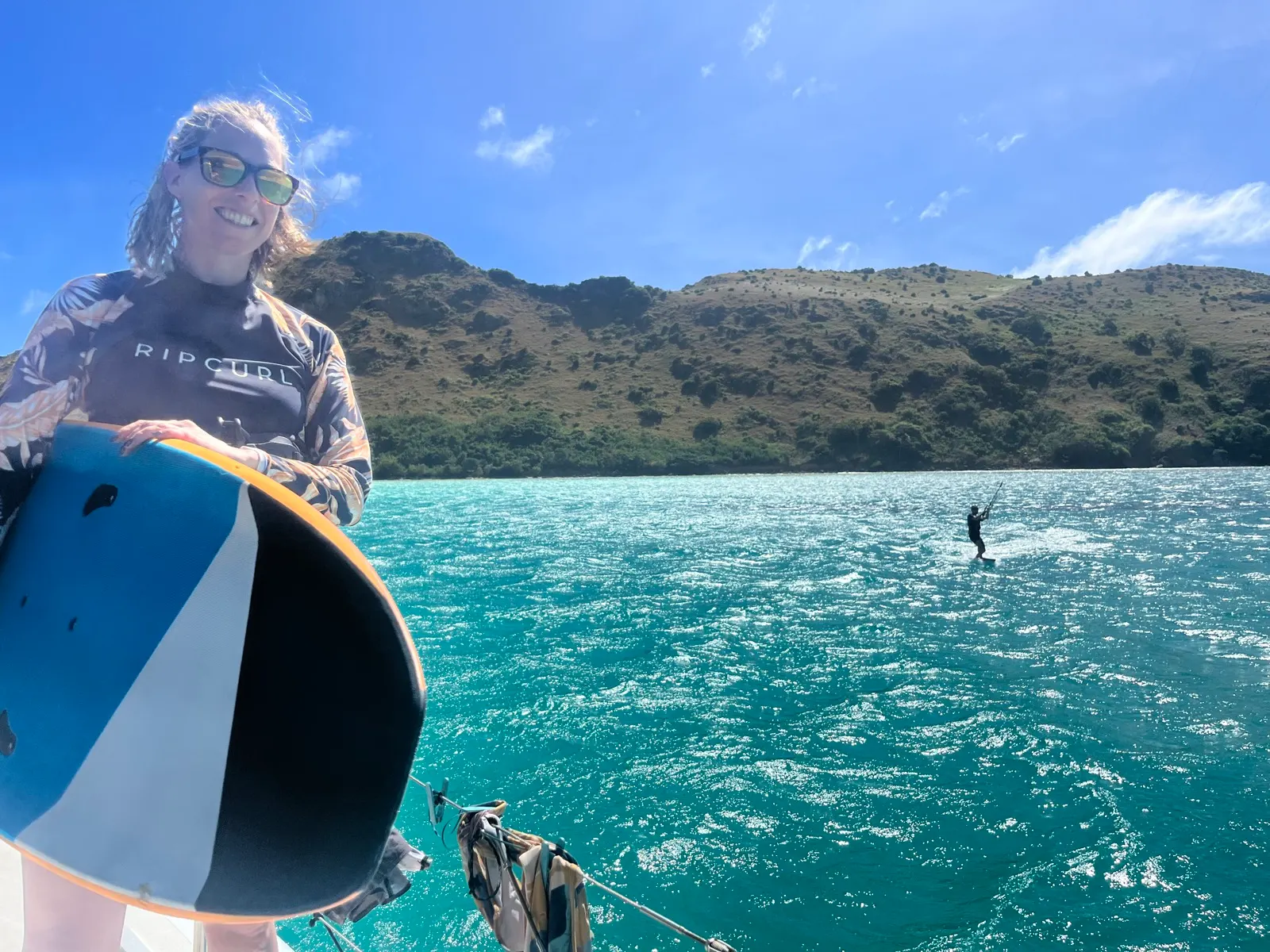 Woman holding kiteboard on boat, kiter riding behind