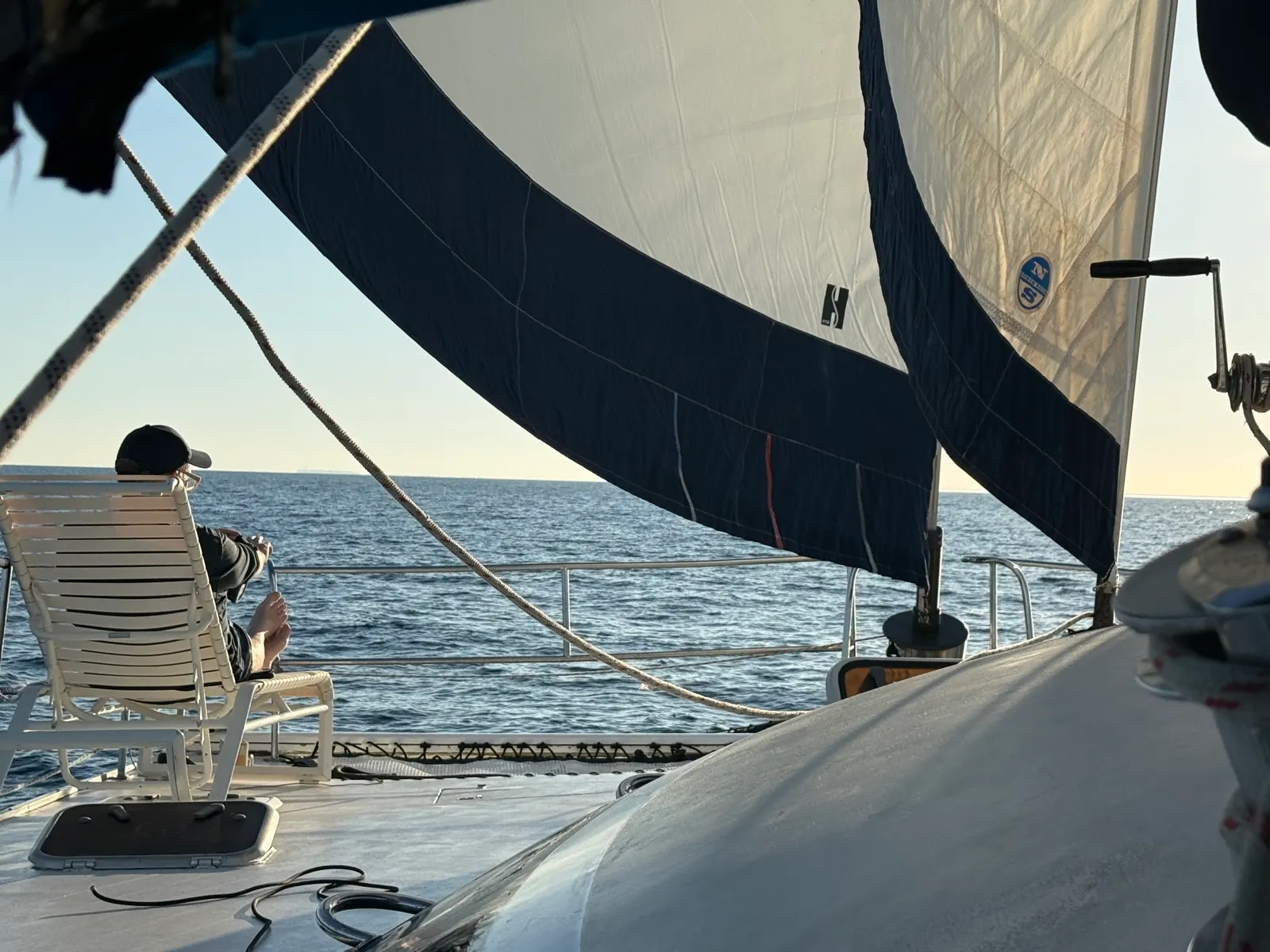 Person relaxing on deck under sails, open water