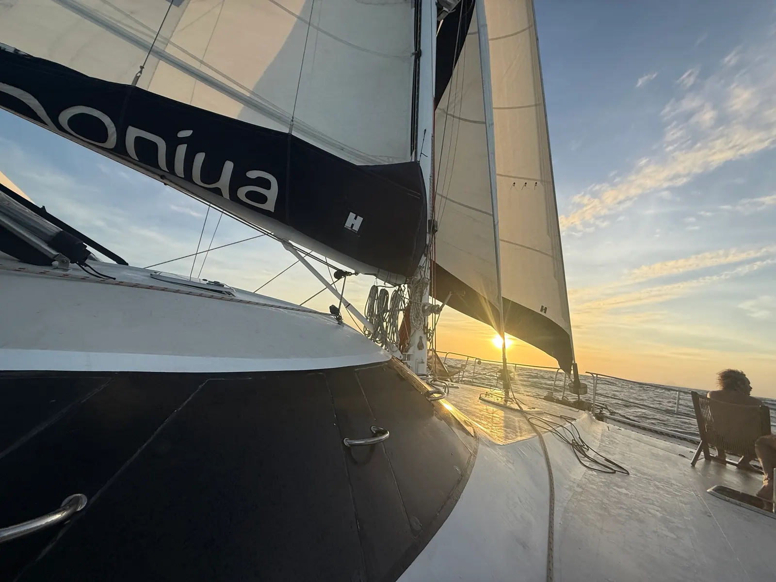 Person seated on deck watching sunset through sails