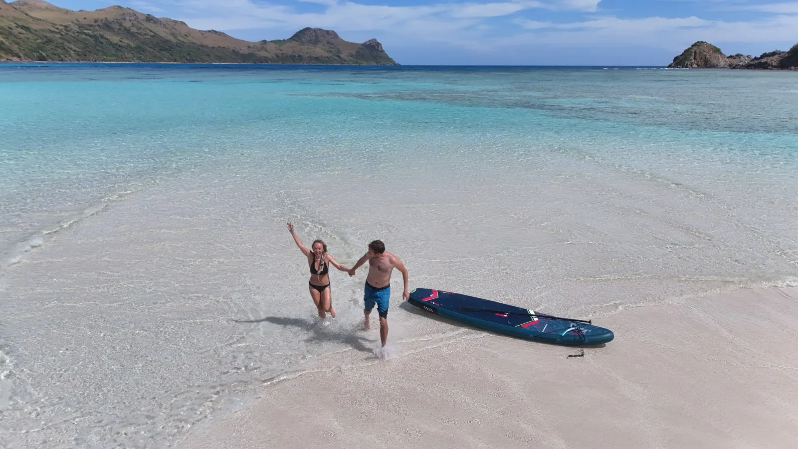 Couple celebrating on a white sandbar, catamaran in distance
