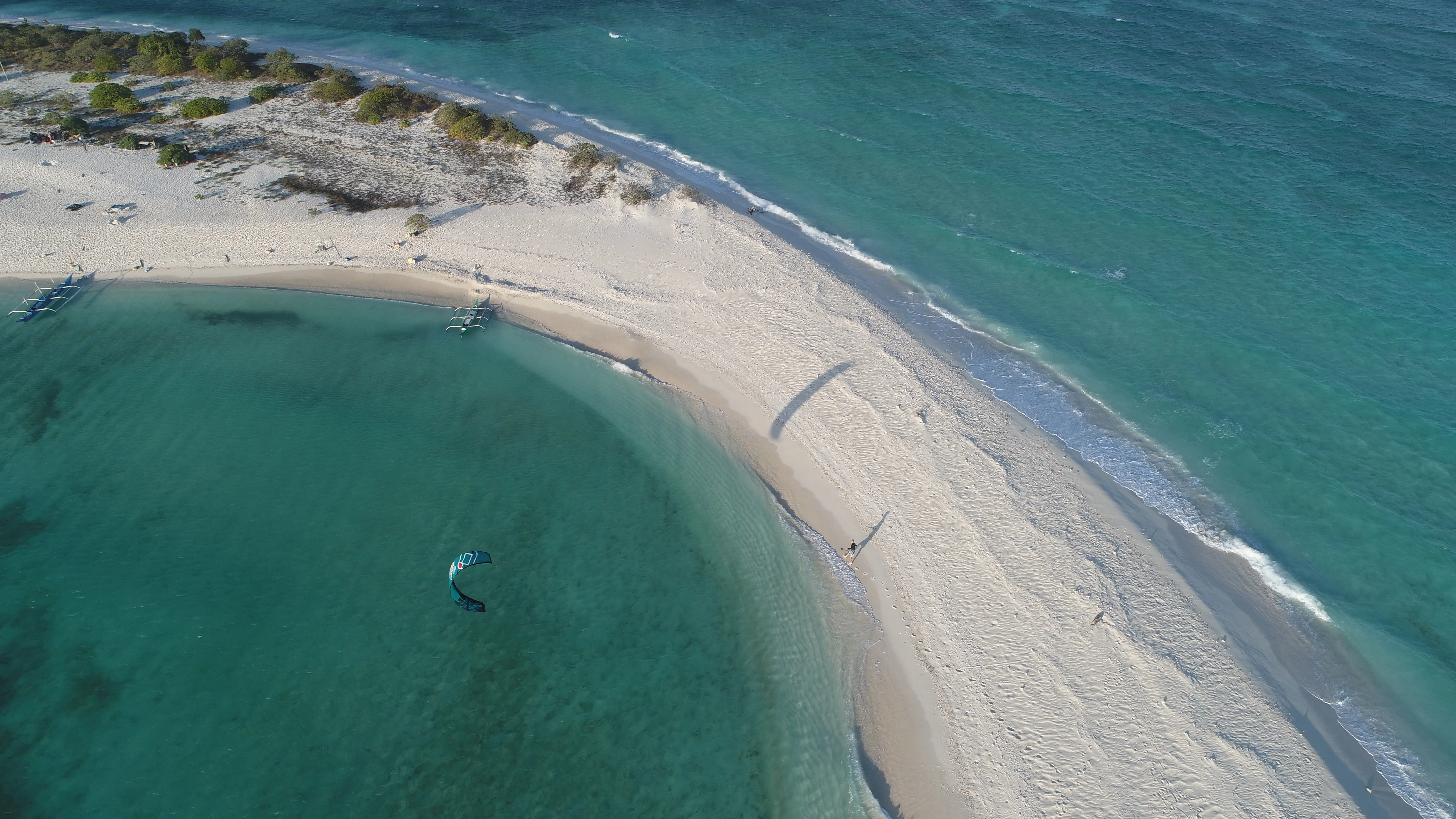 Aerial view of Seco Island's curved sandbar with a dinghy offshore