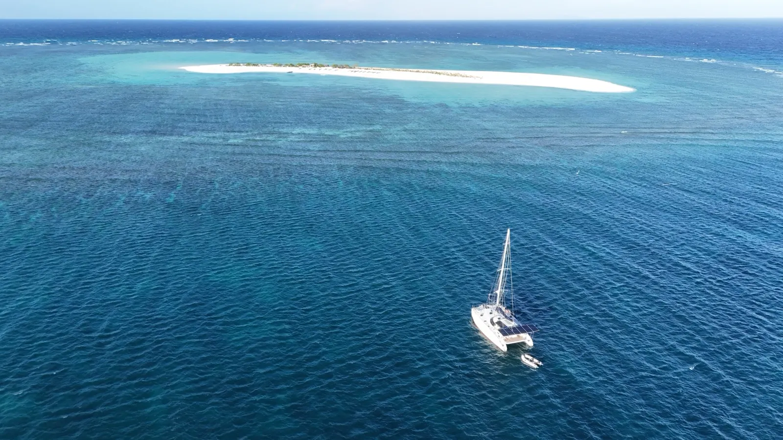 Aerial of long sand spit island with distant kite and boat