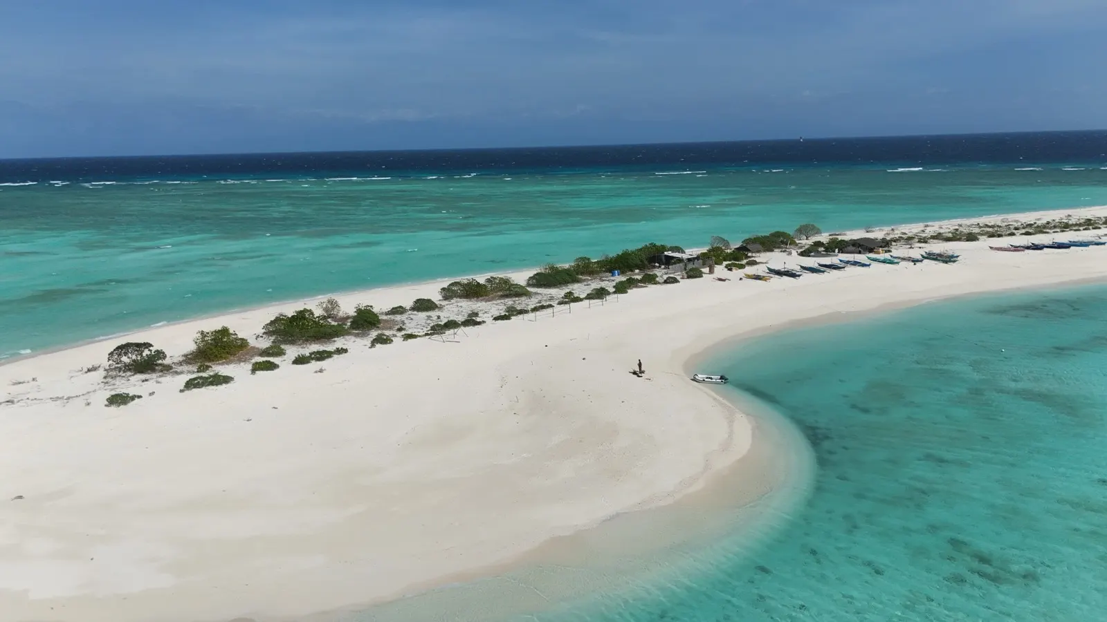 Aerial of sandbar village with fishing boats, person on beach