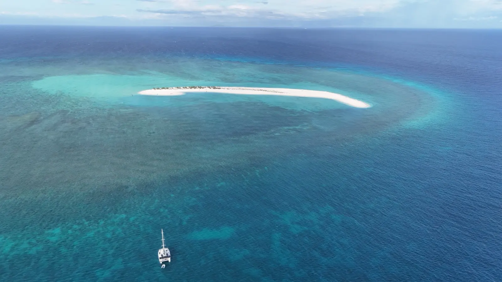 Aerial oval reef island with catamaran approaching