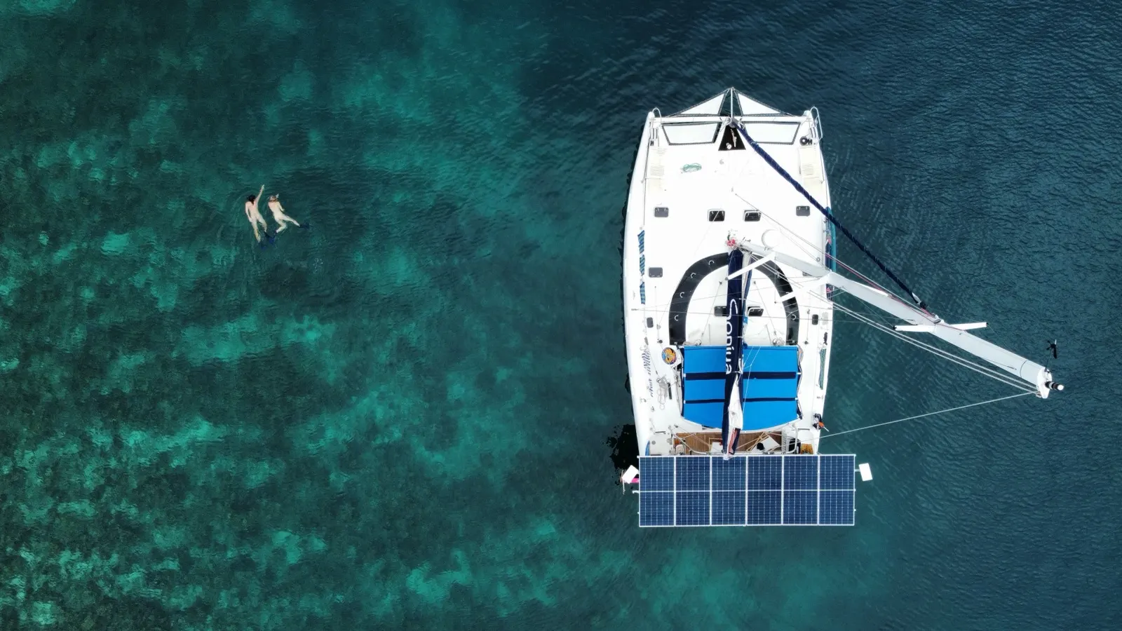 Top-down of catamaran stern with two snorkelers nearby