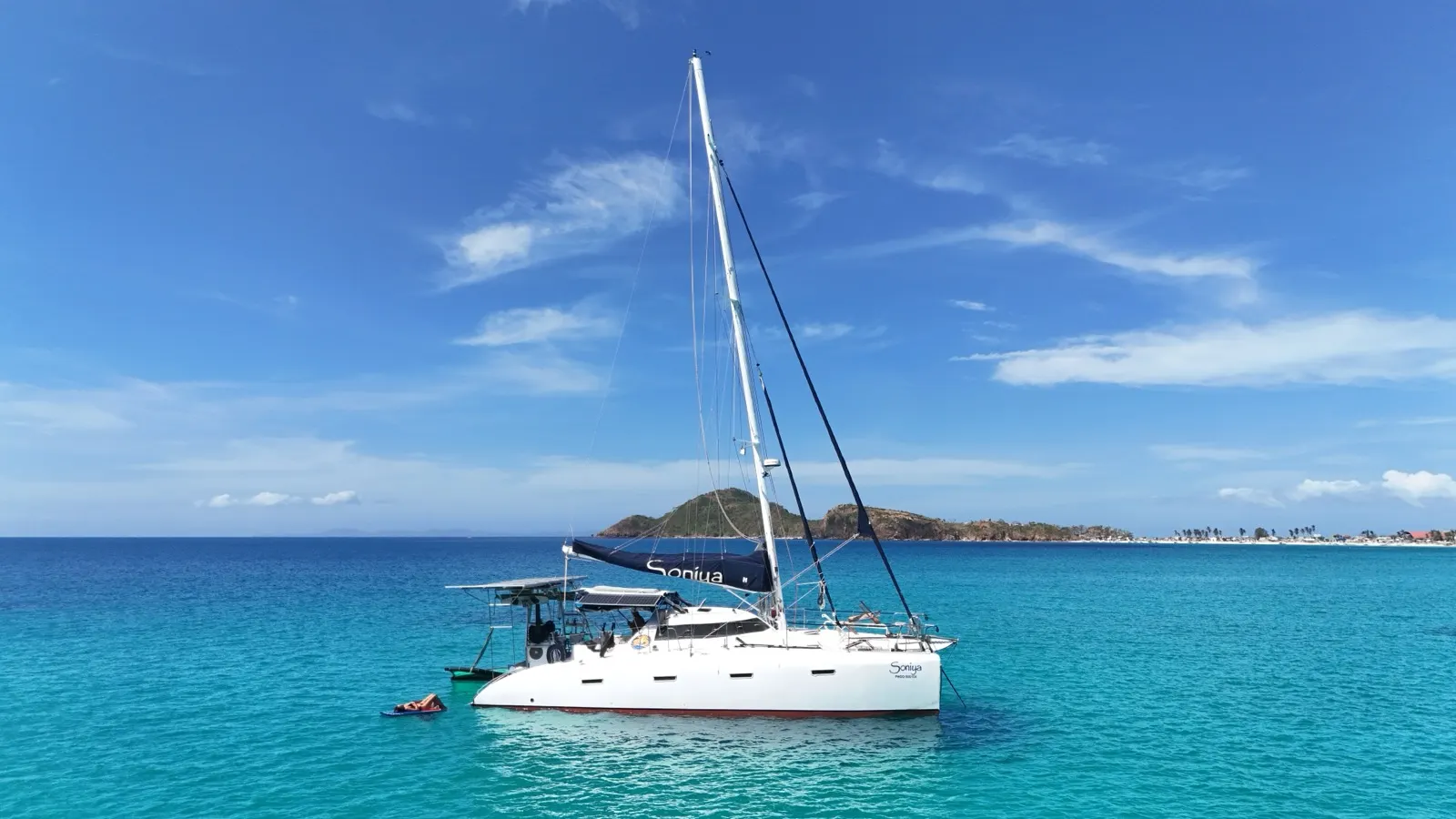 Side profile of catamaran under sail, island backdrop