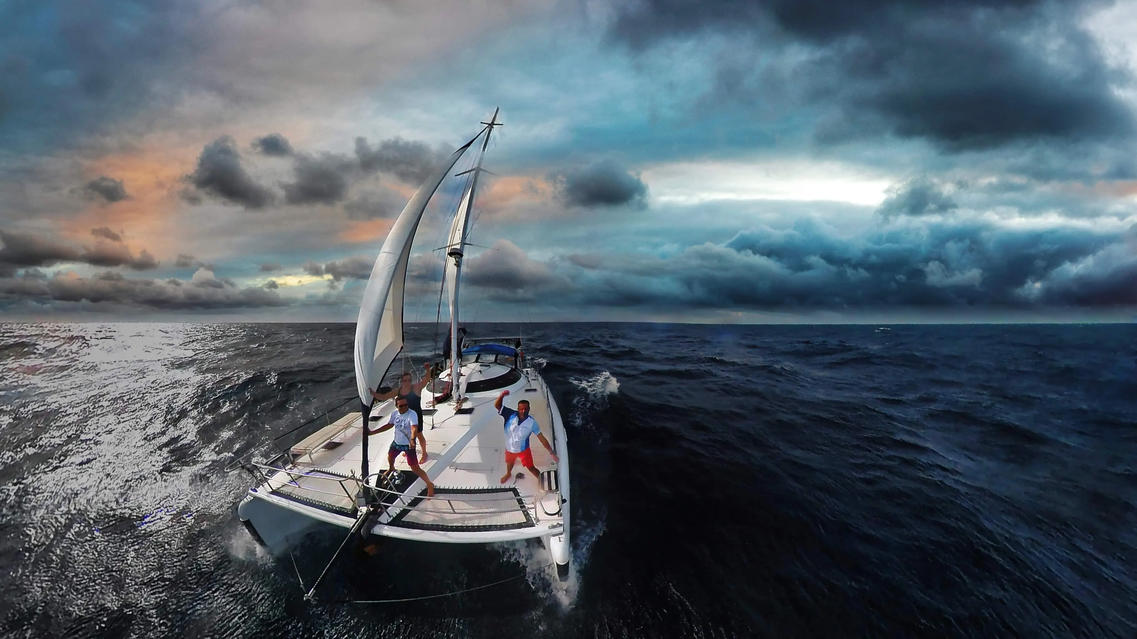 Soniya sailing under a dramatic stormy sky with guests cheering on the bow
